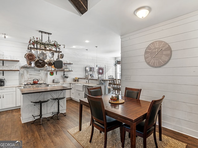 dining space with dark wood-type flooring, wood walls, and sink