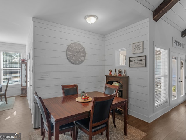 dining area with wood-type flooring, wooden walls, and beamed ceiling