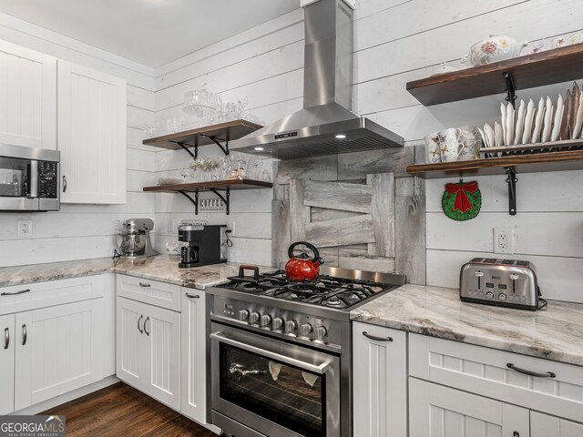 kitchen featuring white cabinetry, light stone countertops, dark hardwood / wood-style floors, appliances with stainless steel finishes, and wall chimney range hood