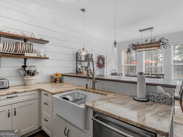 kitchen with stainless steel dishwasher, wood walls, light stone countertops, and hanging light fixtures