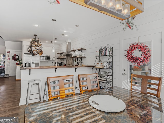 interior space with a kitchen breakfast bar, wall chimney exhaust hood, appliances with stainless steel finishes, kitchen peninsula, and white cabinets