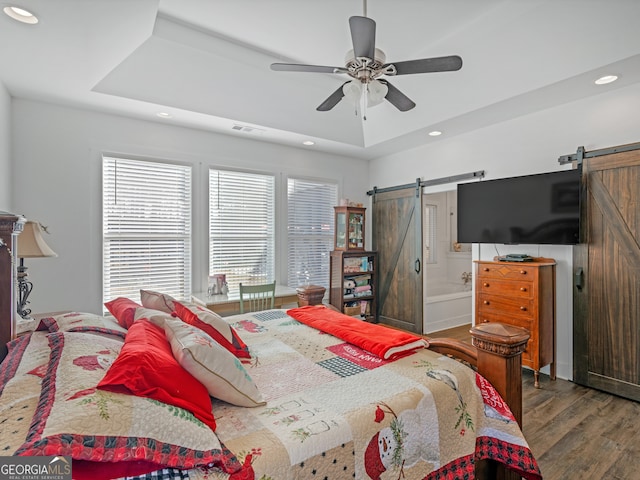 bedroom featuring a barn door, ceiling fan, dark hardwood / wood-style flooring, and ensuite bathroom