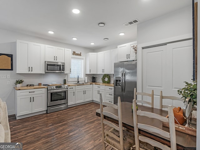 kitchen with butcher block counters, sink, dark wood-type flooring, appliances with stainless steel finishes, and white cabinets