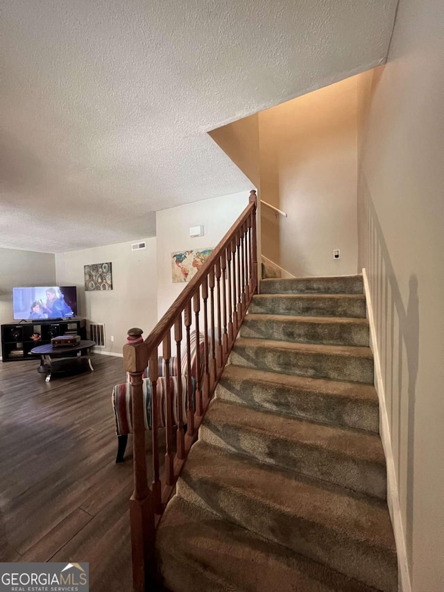 staircase with a textured ceiling and hardwood / wood-style flooring