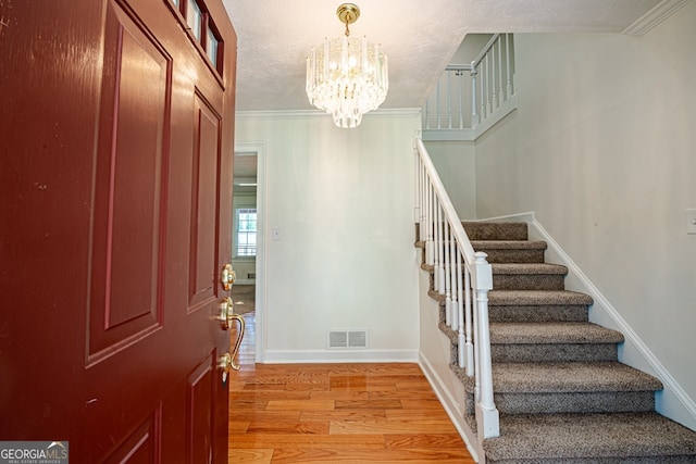 entrance foyer featuring a notable chandelier, light hardwood / wood-style flooring, ornamental molding, and a textured ceiling