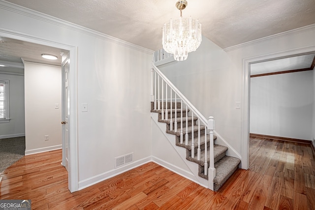 stairs featuring ornamental molding, wood-type flooring, a textured ceiling, and an inviting chandelier