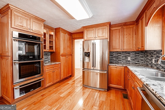 kitchen featuring light wood-type flooring, sink, a textured ceiling, stainless steel appliances, and light stone countertops