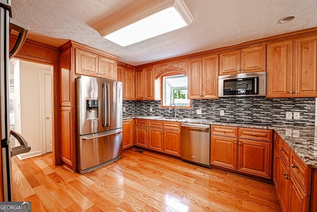 kitchen featuring appliances with stainless steel finishes, decorative backsplash, stone countertops, a textured ceiling, and light hardwood / wood-style flooring