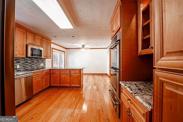 kitchen with appliances with stainless steel finishes, light hardwood / wood-style floors, stone countertops, ceiling fan, and ornamental molding