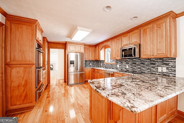 kitchen with light stone counters, stainless steel appliances, kitchen peninsula, and light hardwood / wood-style flooring