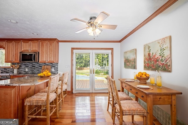 kitchen featuring ceiling fan, light stone counters, backsplash, crown molding, and light hardwood / wood-style floors