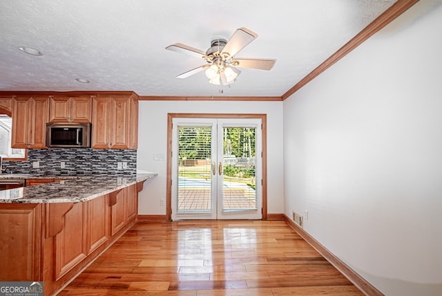 kitchen featuring light wood-type flooring, a textured ceiling, backsplash, light stone countertops, and ceiling fan