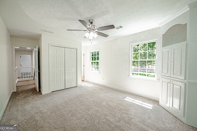 unfurnished bedroom with ceiling fan, light colored carpet, a textured ceiling, and a closet