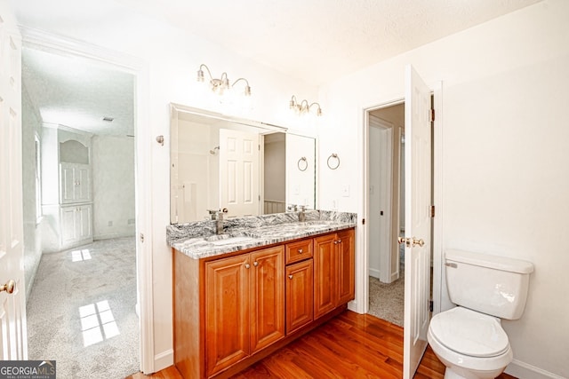 bathroom featuring wood-type flooring, vanity, toilet, and a textured ceiling