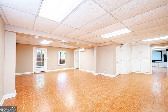 interior space featuring light wood-type flooring, a wall mounted air conditioner, and a paneled ceiling