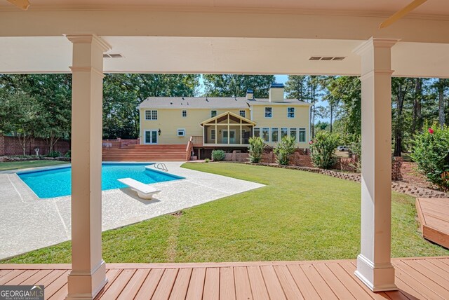 view of swimming pool with a lawn, a diving board, a deck, and a sunroom