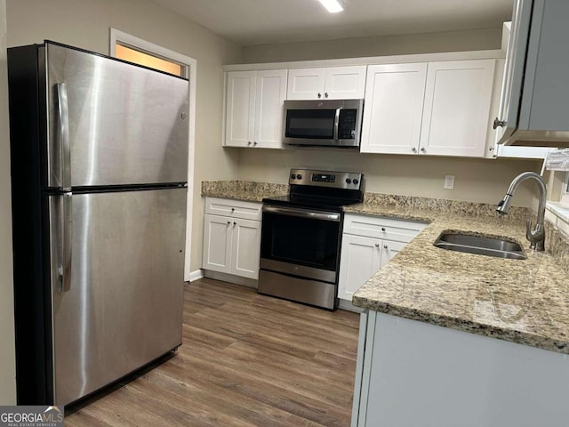 kitchen with stainless steel appliances, sink, hardwood / wood-style flooring, white cabinetry, and light stone counters