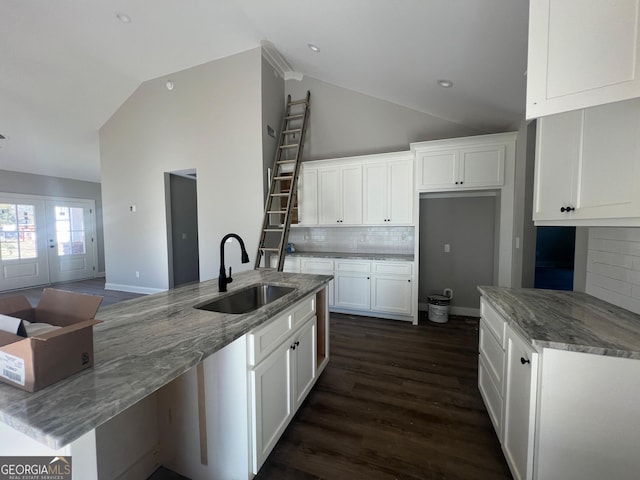 kitchen featuring decorative backsplash, light stone countertops, vaulted ceiling, sink, and white cabinets