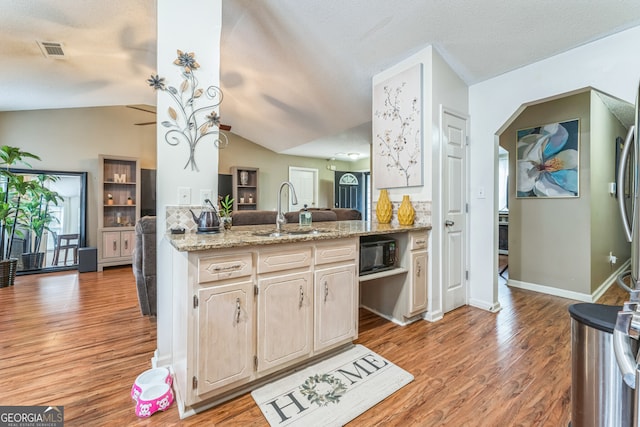 kitchen with light wood-type flooring, kitchen peninsula, sink, light stone countertops, and lofted ceiling