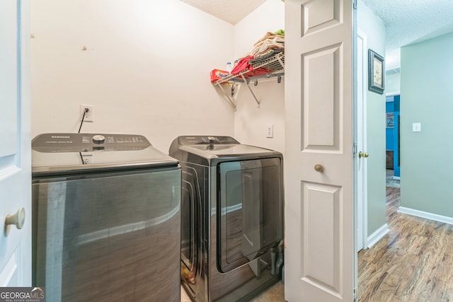 laundry area featuring light wood-type flooring, washing machine and clothes dryer, and a textured ceiling