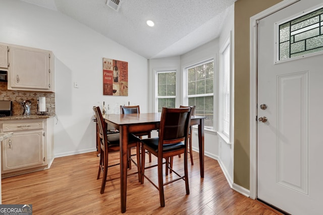 dining room featuring a textured ceiling, light wood-type flooring, and lofted ceiling