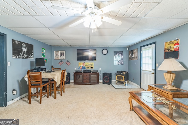 home office with a wood stove, light colored carpet, ceiling fan, and a drop ceiling