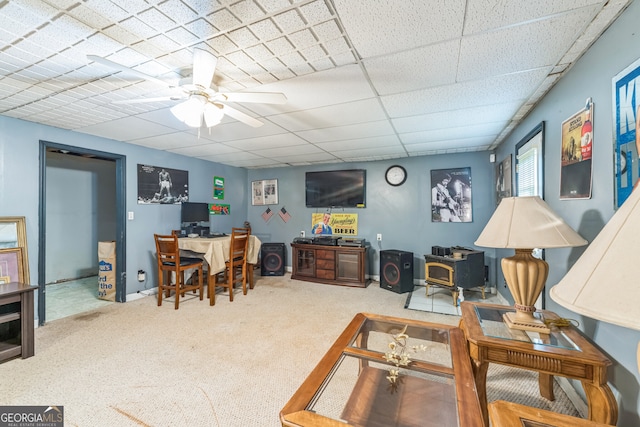 carpeted living room featuring a wood stove, ceiling fan, and a drop ceiling