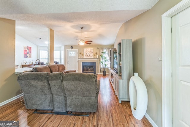 living room featuring a textured ceiling, ceiling fan, wood-type flooring, and vaulted ceiling