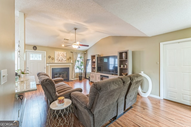 living room featuring vaulted ceiling, a textured ceiling, light hardwood / wood-style flooring, and ceiling fan