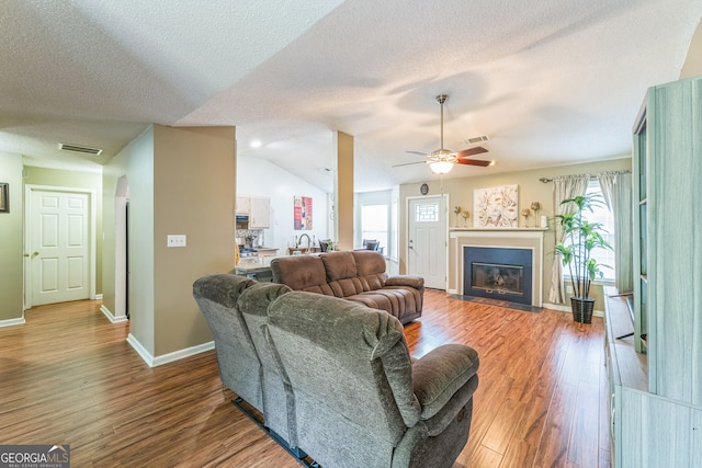 living room featuring ceiling fan, hardwood / wood-style flooring, vaulted ceiling, and a textured ceiling