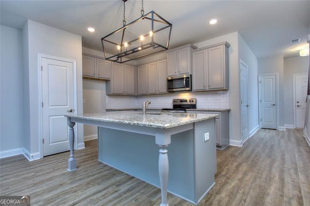 kitchen featuring gray cabinetry, appliances with stainless steel finishes, light hardwood / wood-style floors, an island with sink, and pendant lighting