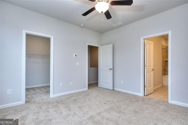 unfurnished bedroom featuring light carpet, ensuite bath, ceiling fan, a closet, and a spacious closet