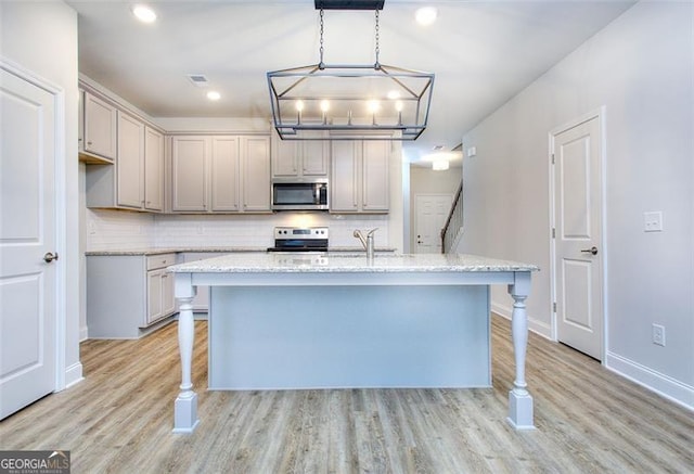 kitchen with light wood-type flooring, decorative light fixtures, appliances with stainless steel finishes, and light stone countertops