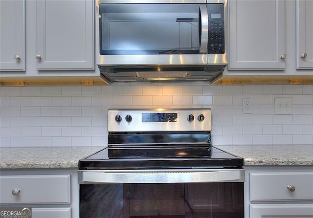 kitchen featuring stainless steel appliances, light stone counters, backsplash, and white cabinets