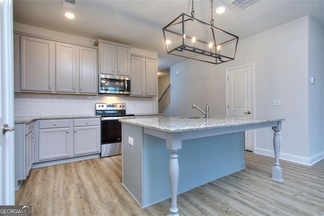 kitchen featuring a kitchen island with sink, a kitchen bar, decorative light fixtures, appliances with stainless steel finishes, and light hardwood / wood-style floors