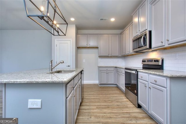 kitchen featuring decorative light fixtures, stainless steel appliances, sink, gray cabinets, and light wood-type flooring