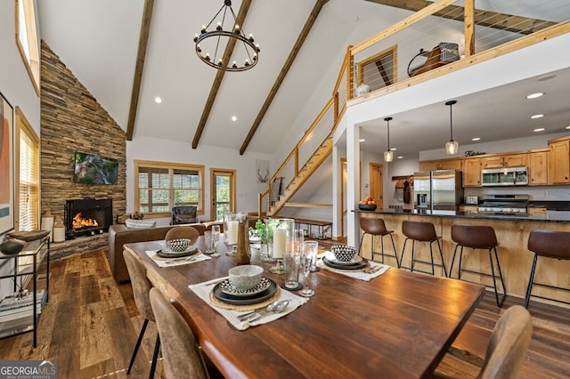 dining area with dark wood-type flooring, high vaulted ceiling, a stone fireplace, beamed ceiling, and a notable chandelier