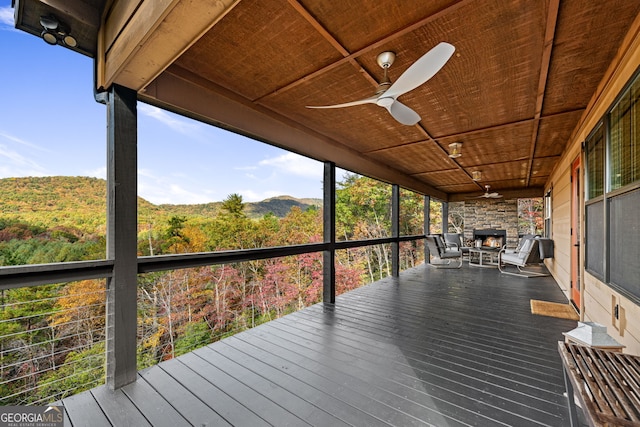 unfurnished sunroom featuring ceiling fan, an outdoor stone fireplace, and wood ceiling