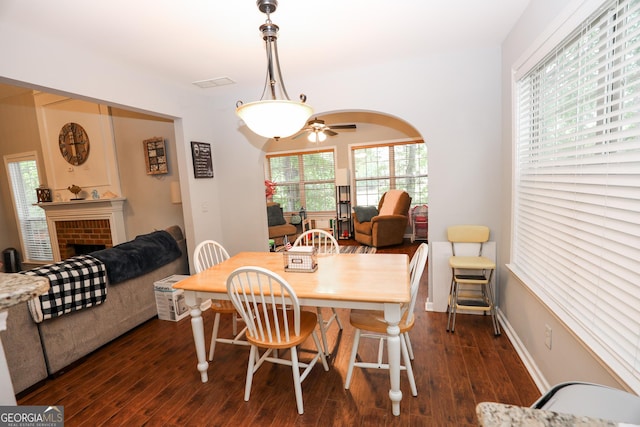 dining room featuring dark wood-type flooring, baseboards, visible vents, a ceiling fan, and a fireplace