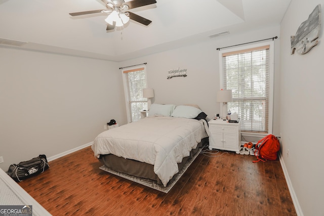 bedroom with baseboards, visible vents, wood finished floors, and a raised ceiling