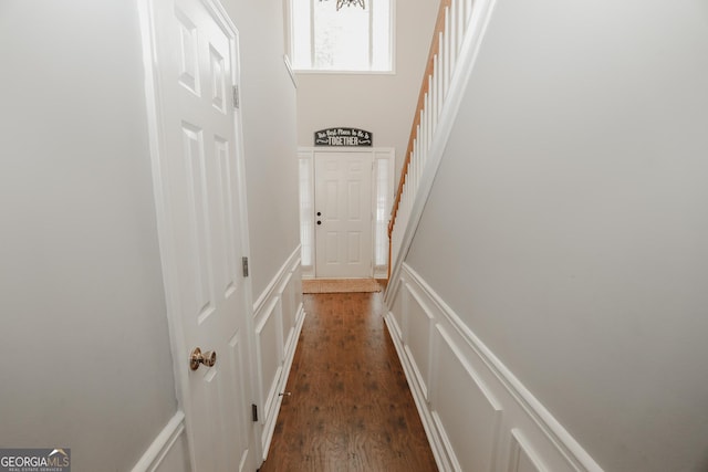 hall with a decorative wall, a towering ceiling, dark wood-type flooring, and wainscoting