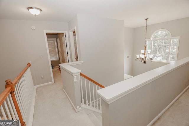 hallway with light colored carpet, an upstairs landing, baseboards, and an inviting chandelier