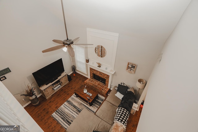 living room featuring baseboards, wood finished floors, ceiling fan, and a brick fireplace