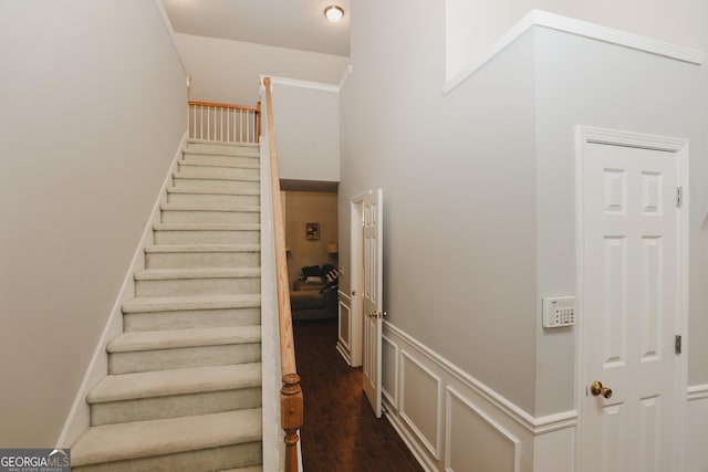 staircase with a decorative wall, wood finished floors, and wainscoting