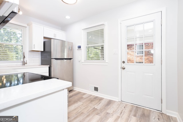 kitchen featuring a healthy amount of sunlight, stainless steel fridge, white cabinetry, and light hardwood / wood-style flooring