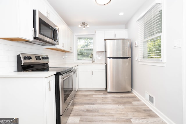 kitchen with stainless steel appliances, white cabinetry, light hardwood / wood-style floors, and a healthy amount of sunlight