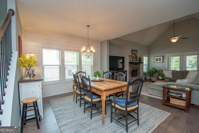 dining area with ceiling fan with notable chandelier, dark hardwood / wood-style flooring, lofted ceiling, and a stone fireplace