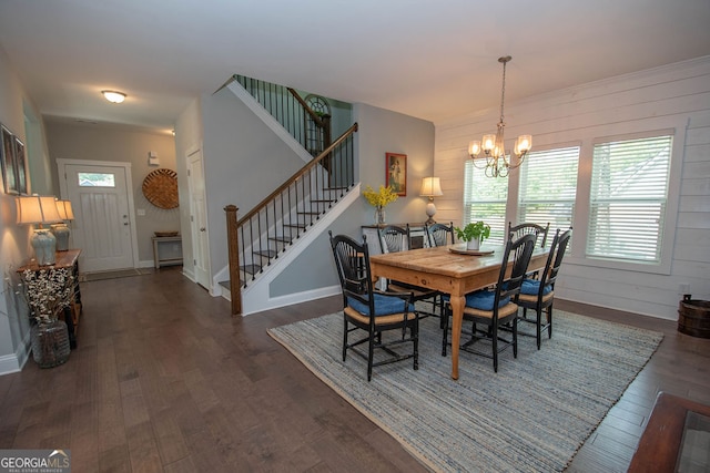 dining space featuring dark wood-type flooring, wood walls, and an inviting chandelier