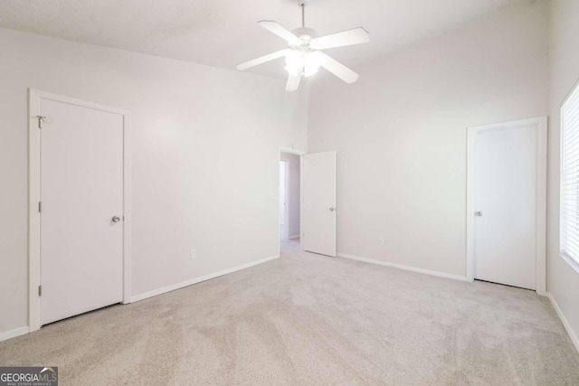 unfurnished bedroom featuring baseboards, carpet floors, high vaulted ceiling, and a ceiling fan