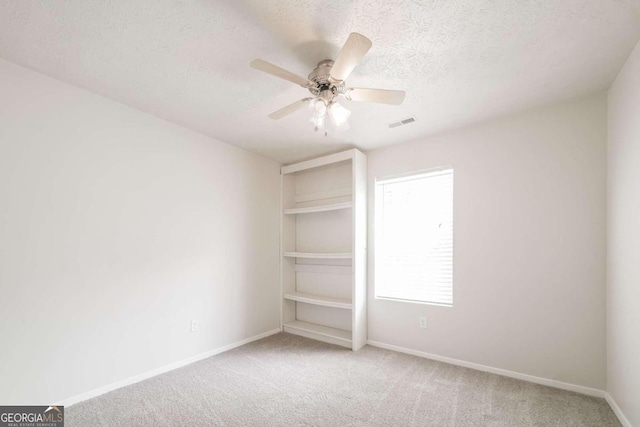 carpeted spare room featuring visible vents, built in features, a textured ceiling, baseboards, and ceiling fan